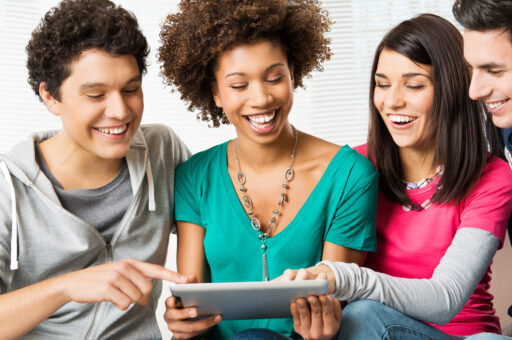 Ein Foto von 4 Personen, die vor einem Tablet sitzen. Sie lachen.