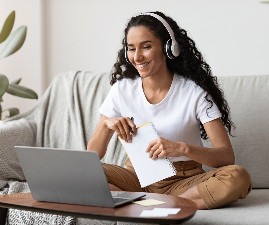 Eine Frau die auf dem Sofa vor einem Laptop sitzt. Sie hat Kopfhörer auf.
