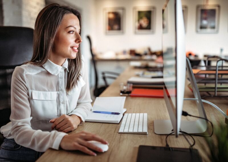 Eine Frau schaut auf ihren Computerbildschirm und lächelt.