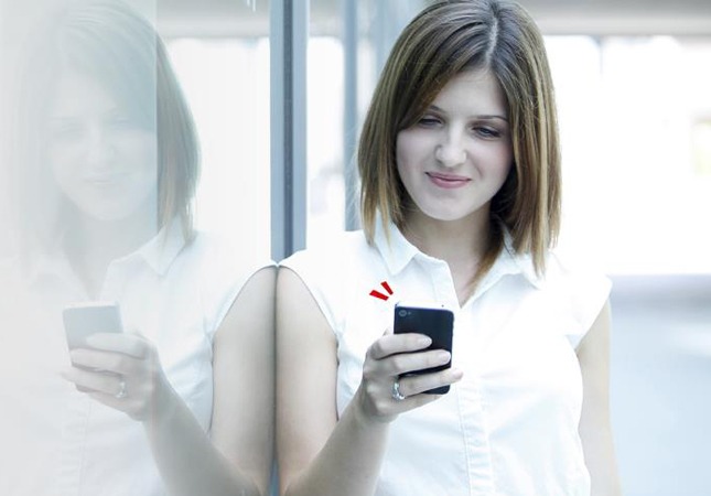 Junge Frau in weißem Shirt schaut auf ihr Smartphone.