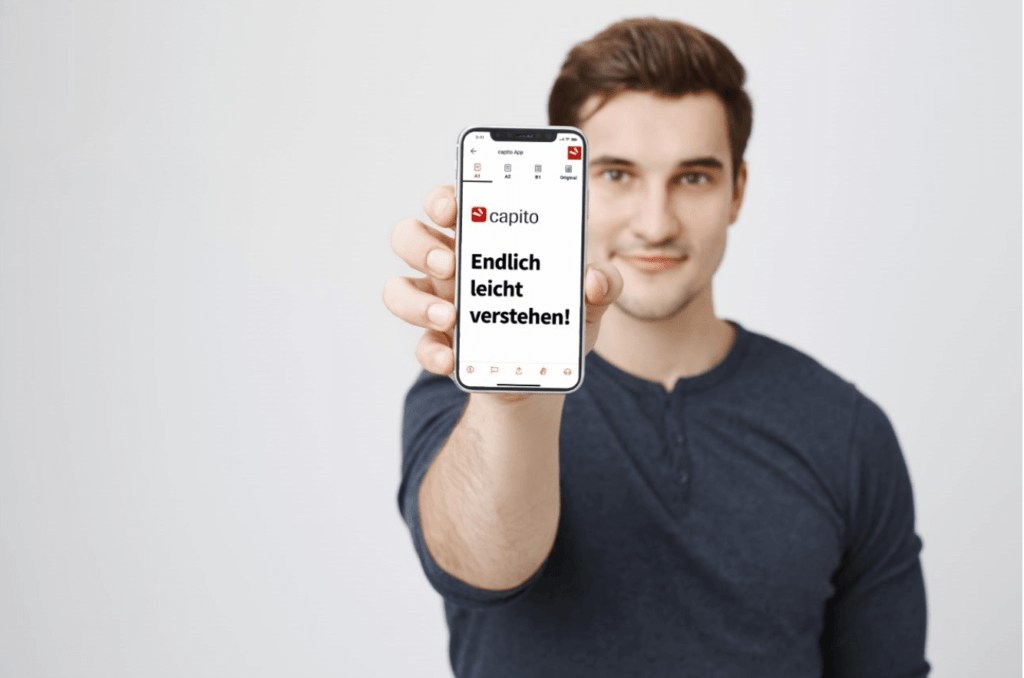 Portrait of young european model advertising new capito app on smartphone, showing it to camera, standing over gray background. capito makes complicated texts easy understandable.