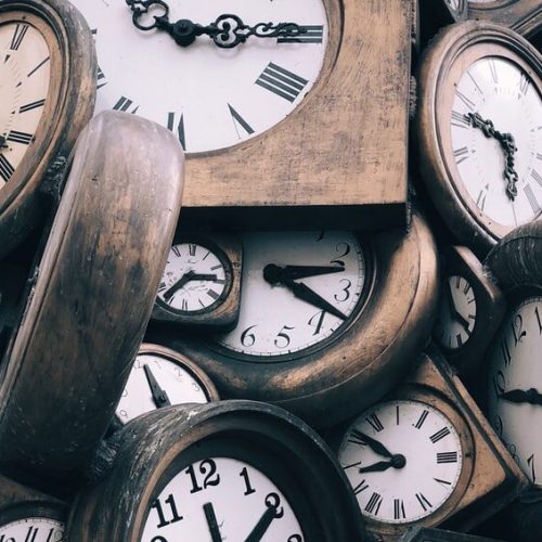 Arbeitszeiten erfassen - E-Learning - Viele Uhren mit Holzumrahmung liegen auf einem Haufen.