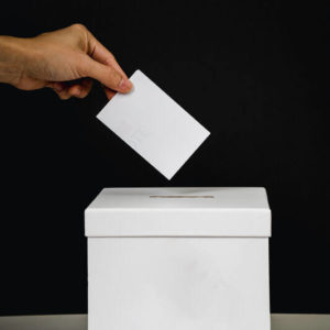 Hand steckt Zettel in Wahlurne dank hife der Wahlanleitung in leichter Sprache von capito